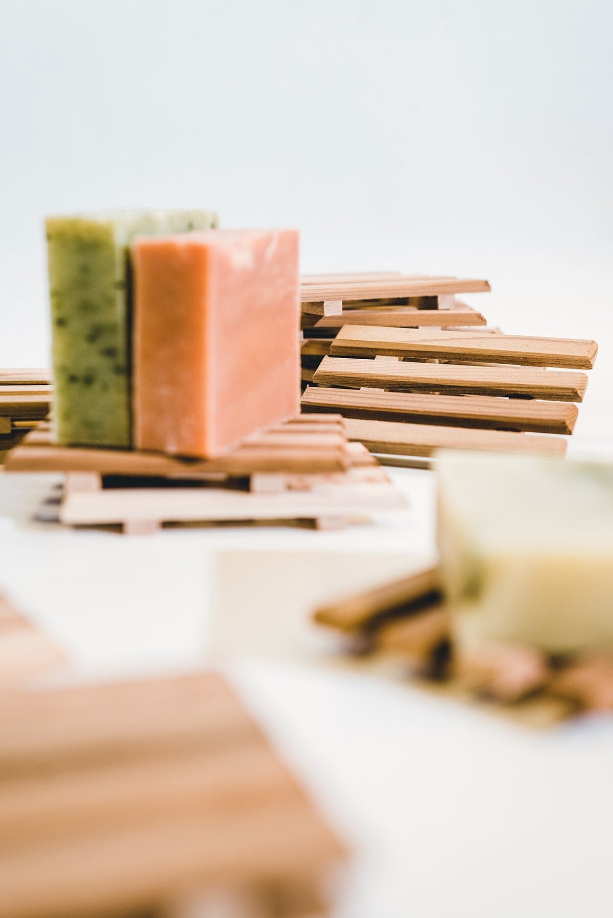 Two bars of soap from Iron Lion Soap sitting on an wooden soap tray surrounded by stacks of wood soap trays and bars of soap.